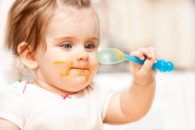 little girl feeding from a spoon on blue chair eat baby child